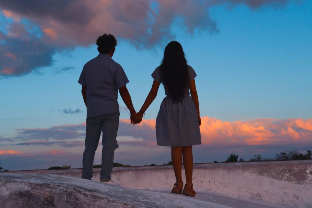 A couple holding hands while standing on a rooftop with a vibrant sunset sky.