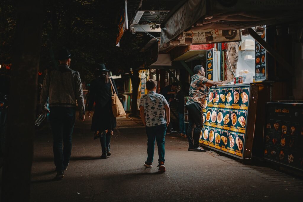 Busy evening at a street market with food stalls and pedestrian activity.