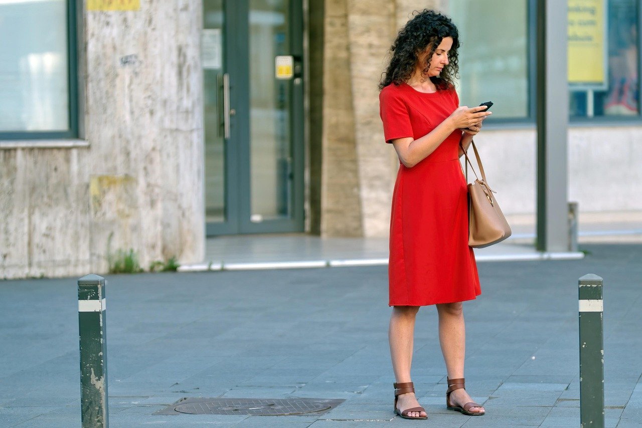 woman, red dress, phone, purse, bag, young, building, urban, town, person, sidewalk, snapshot, street photography, looking, s