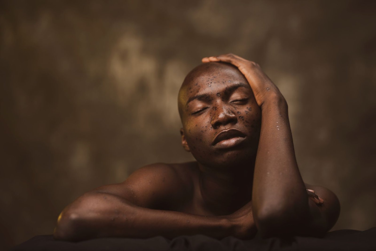 A serene studio portrait of a shirtless black man with freckles and closed eyes.