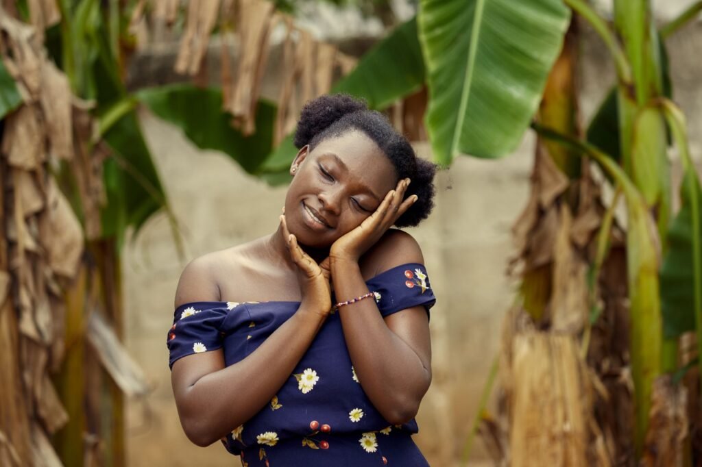 A young African woman poses peacefully outdoors in Ghana surrounded by lush green banana leaves.