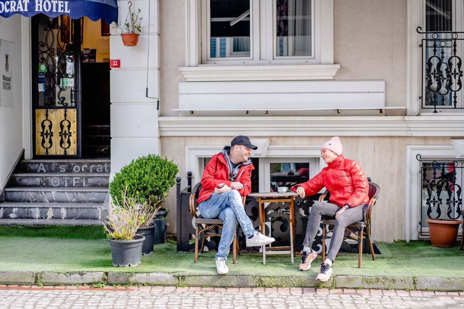 A couple conversing outside a hotel café, enjoying a relaxed moment on a sunny day.