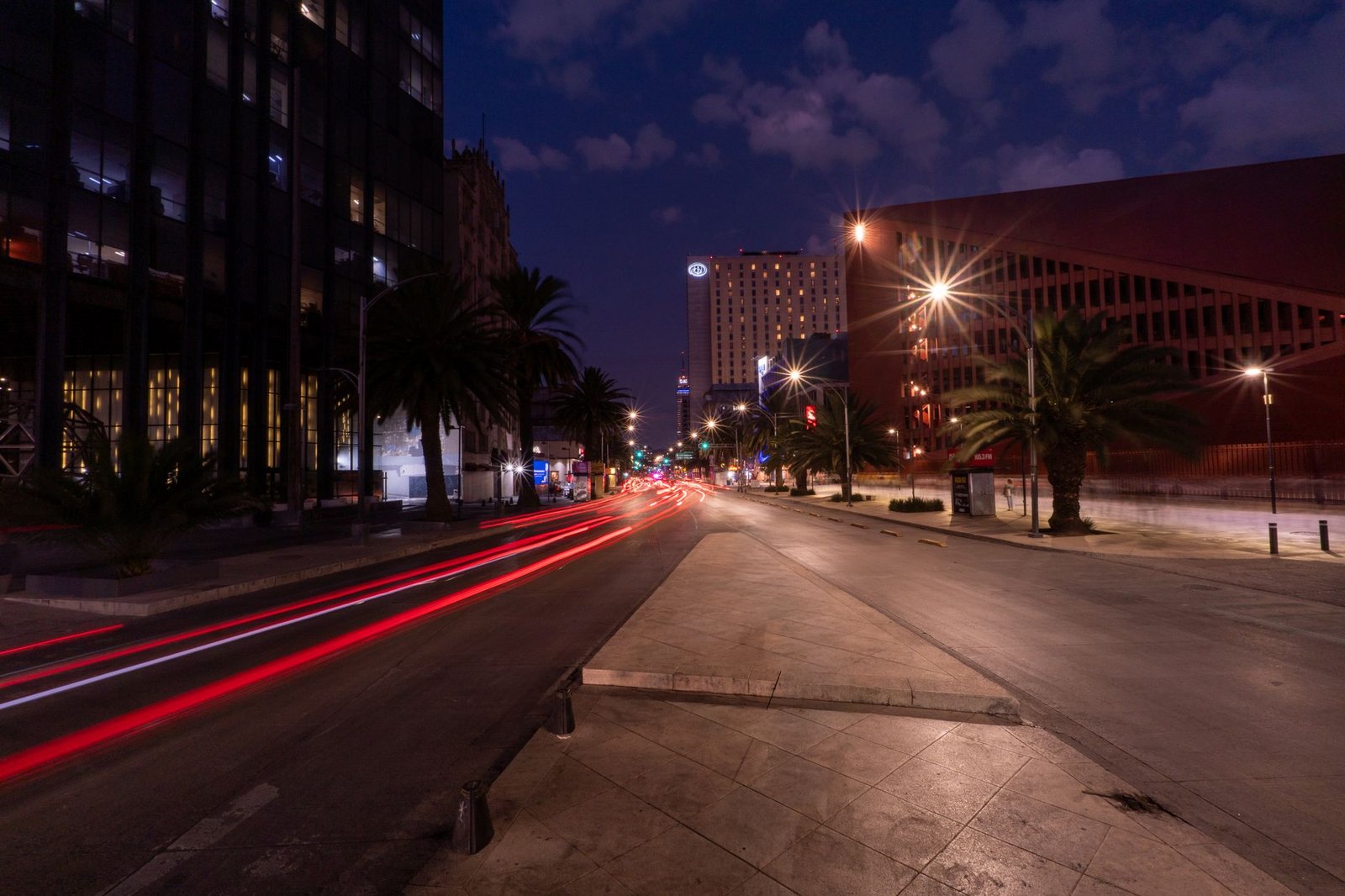 Capture of a bustling Mexico City street at night, featuring prominent light trails and architectural details.