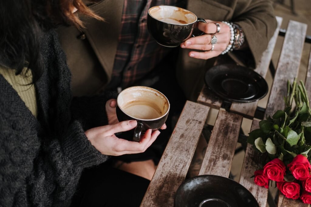 From above of crop unrecognizable couple with coffee interacting at cafe table with blooming flowers on weekend