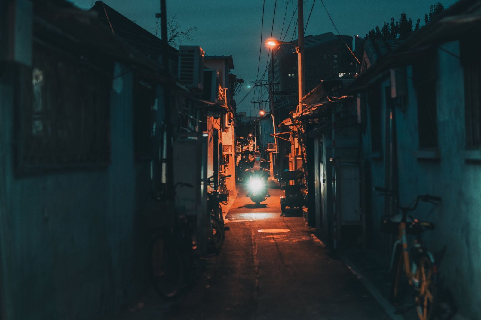 Moody night scene in a Beijing alley with a motorcycle and ambient streetlights.