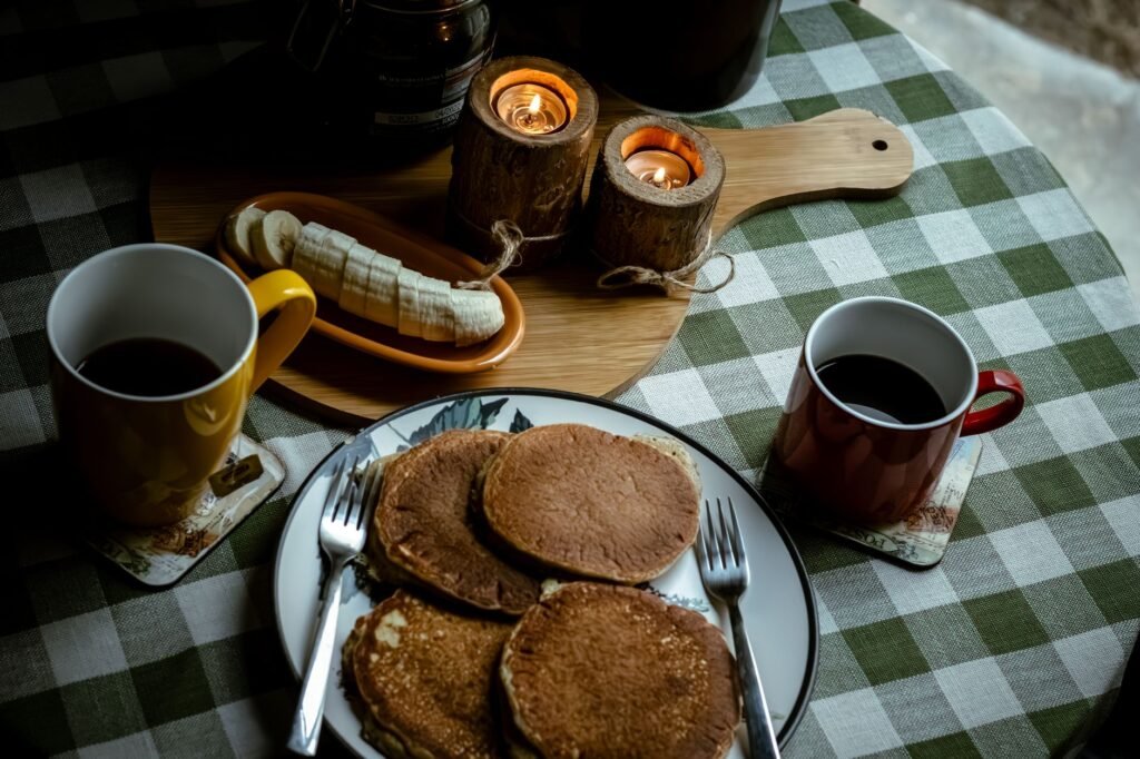 A cozy breakfast setup with pancakes, coffee, and candles on a plaid tablecloth.