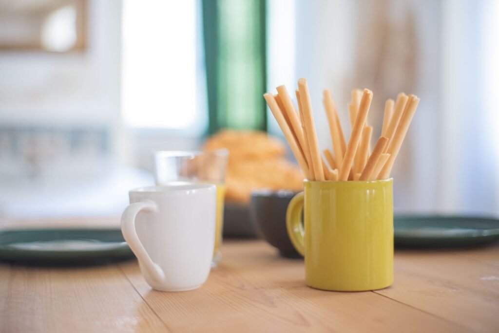 A close-up of a cozy breakfast setup with mug and breadsticks on a wooden table.