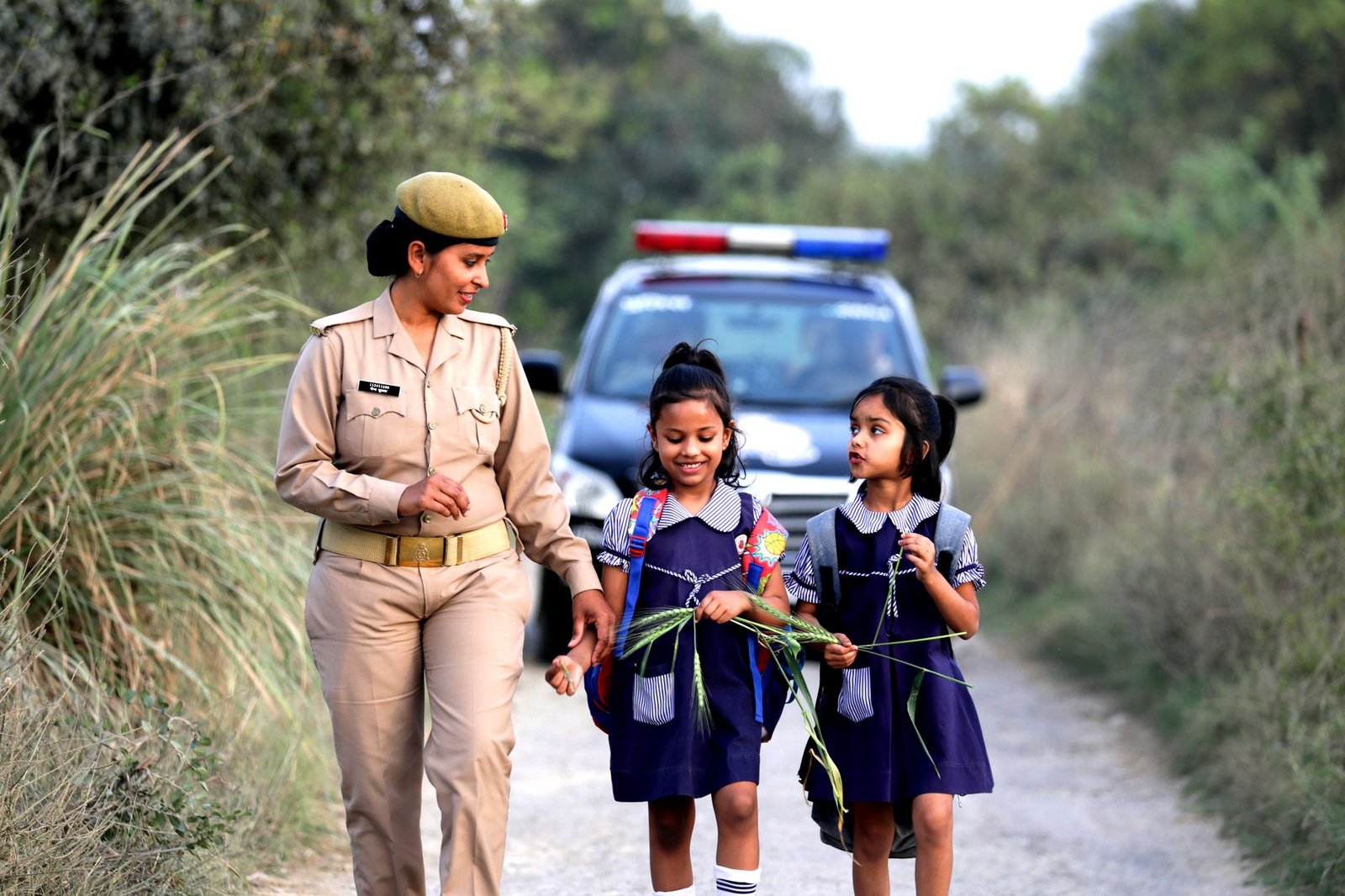 A police officer escorts two school girls through a nature path, promoting safety.
