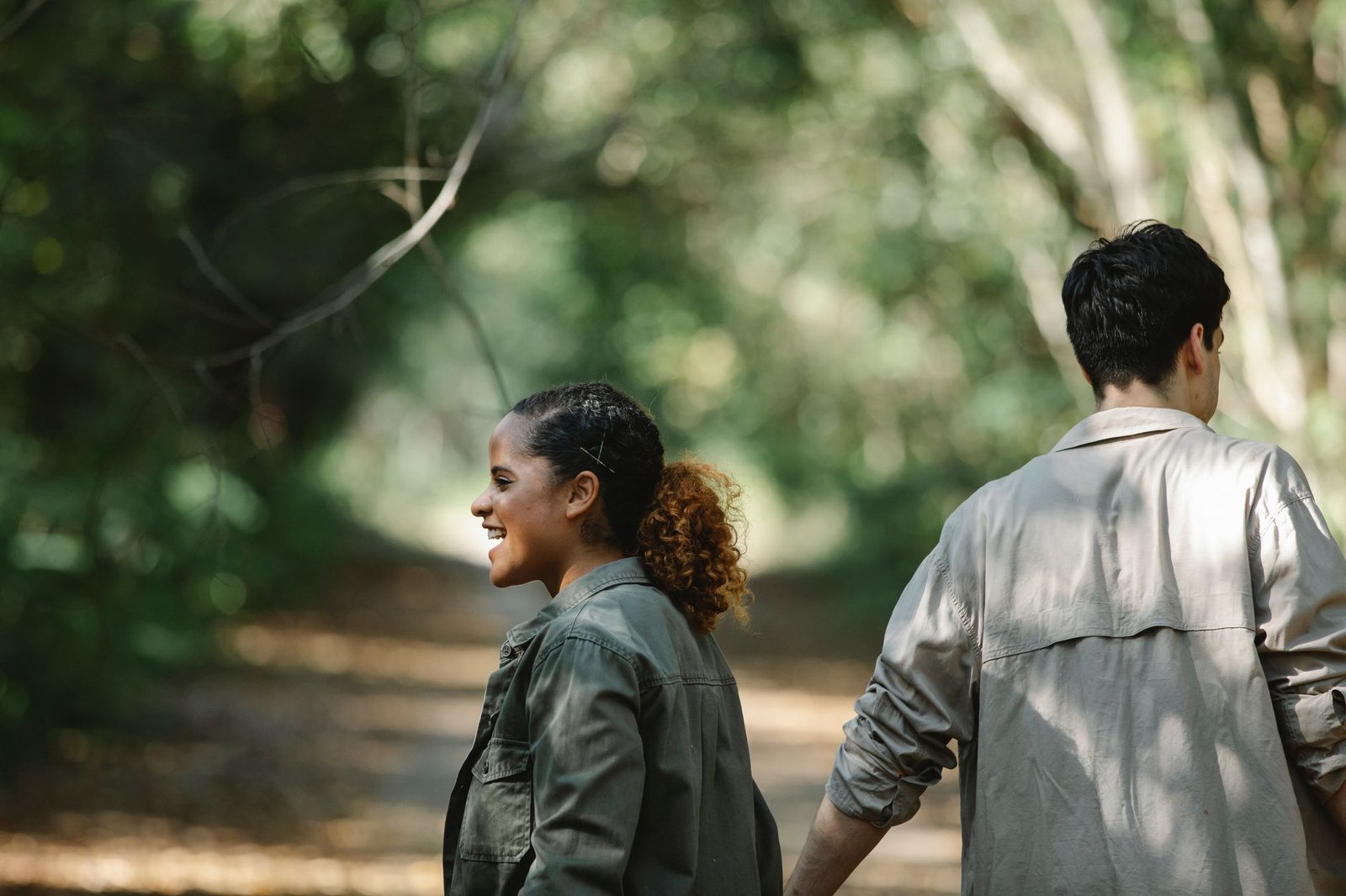 Back view of delighted young multiethnic couple walking in park and holding hands while having date