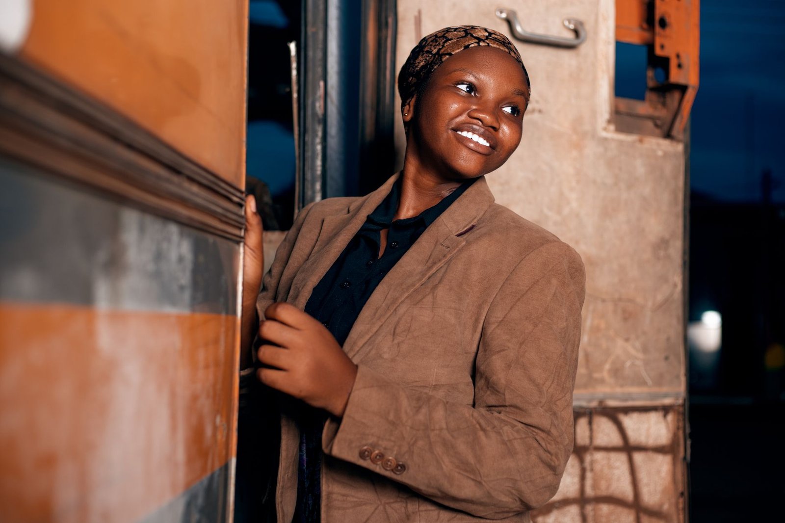 A woman in a brown jacket smiles as she boards a bus at night in Ghana.