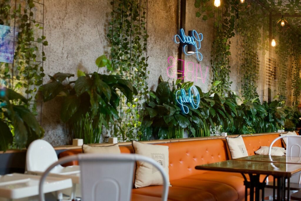 A stylish cafe in West Java, Indonesia featuring vibrant plants, a neon sign, and modern decor.