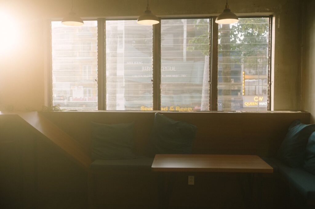 Warm sunlit interior view of a cozy café with pillows and tables by the window.